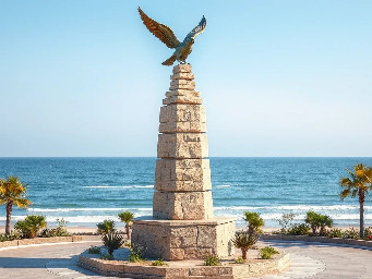 A 5-meter tall majestic sculpture made of stacked natural stones, featuring a prominent hexagonal base structure with a 6-meter diameter. At the very top, a beautifully sculpted, large-sized bronze dove is captured in mid-flight, symbolizing peace and freedom. The monument is situated in a public park right along the scenic beachfront of Sihanoukville, Cambodia. The base is surrounded by a lush coastal garden with native salt-tolerant plants and beach vegetation. Bright daylight, clear blue sky, soft ocean waves in the background, photorealistic, architectural rendering style, highly detailed stone and polished metal textures, 8k resolution.